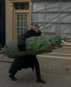 a woman walking down the street carrying a large christmas tree