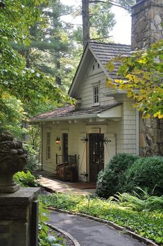 a white house surrounded by greenery and trees in the woods with a path leading to it