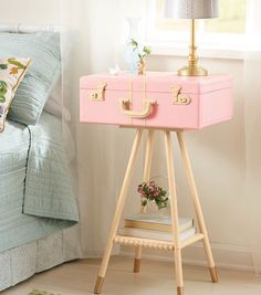 a pink suitcase sitting on top of a wooden stand next to a bed with pillows