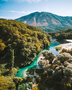 an aerial view of a river surrounded by trees and mountains in the distance with blue water