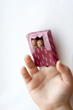 a hand holding up a small pink box with two dolls in it's center