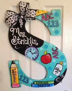 a door hanger that has the letter s painted on it with school supplies around it