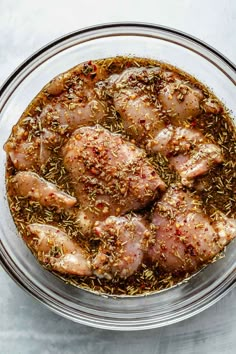 a glass bowl filled with cooked chicken and seasoning on top of a white table