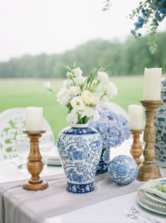 blue and white vases with flowers in them on a table set for an outdoor dinner