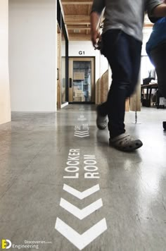 a man walking down a hallway with an arrow painted on the floor next to him