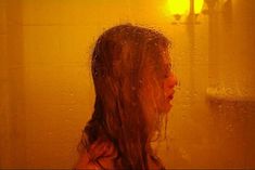 a girl standing in front of a shower with water on her face and hair blowing back