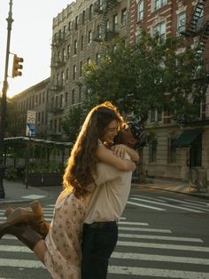 a man and woman walking across a cross walk holding each other's arms as the sun goes down