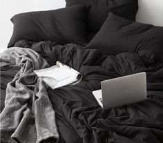 an open laptop computer sitting on top of a black bed covered in blankets and pillows