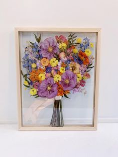 a vase filled with lots of colorful flowers sitting in front of a framed wall hanging