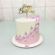 a white and pink birthday cake with butterflies on top, sitting on a table in front of a tile wall