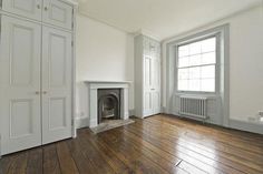 an empty living room with wood floors and white walls, including a fireplace in the corner