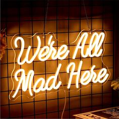 a neon sign that says we're all mad here hanging from the side of a wall