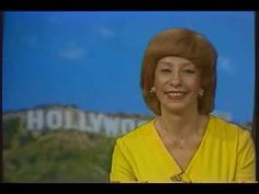 an older woman is smiling in front of a hollywood sign on the television screen, wearing a yellow dress