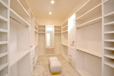 an empty walk - in closet with white shelves and drawers, including a footstool