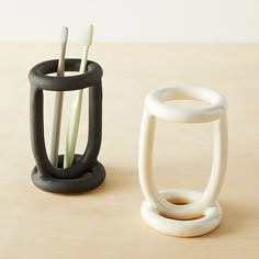 two toothbrush holders sitting next to each other on a wooden table with white and black handles