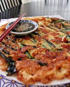 a pizza with some chopsticks on top of it next to a small bowl