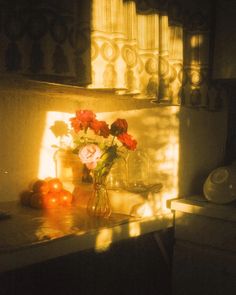 the sun shines on some flowers in a vase and fruit sitting on a counter