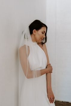 a woman in a white wedding dress leaning against a wall with her arms crossed and looking down