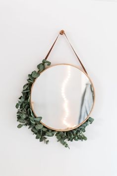 a round mirror hanging on the wall with greenery