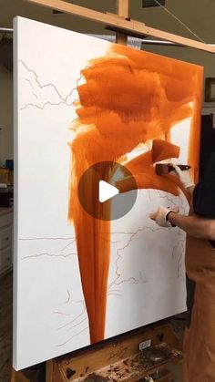 a man is painting on an easel with orange paint