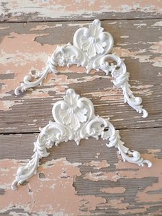 two white ornate brackets on an old wooden surface