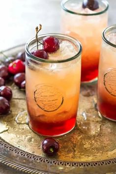 two glasses filled with liquid and cherries on a tray