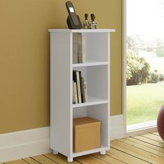 a white book shelf sitting in front of a window next to a red ball and vase