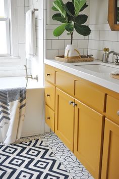 a bathroom with yellow cabinets and black and white floor tiles, a potted plant in the corner