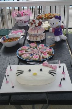 a table topped with lots of cakes and desserts next to a cat shaped cake