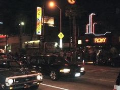 cars are driving down the street at night in front of neon signs and advertisements on buildings