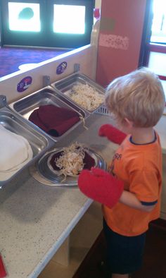 a little boy standing in front of a kitchen counter with food on the trays