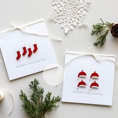 two cards with christmas decorations on them next to pine cones and evergreen branches, one is red and the other is white