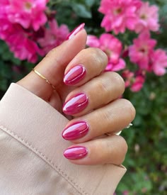 a woman's hand with pink nail polish and gold ring on her finger, in front of flowers