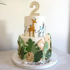 a two tiered cake decorated with jungle leaves and giraffes