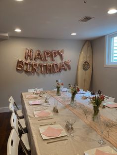 a long table with place settings and flowers on it in front of a happy birthday sign