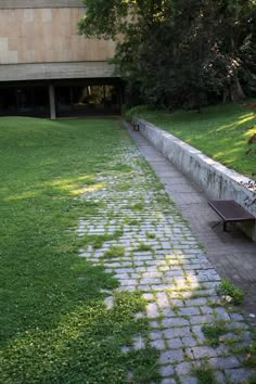 an empty bench sitting in the middle of a grassy area next to a stone wall