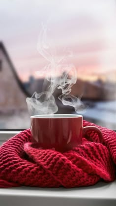 a cup of coffee is sitting on a window sill with a red blanket around it