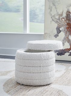 a white ottoman sitting on top of a rug in front of a large art piece