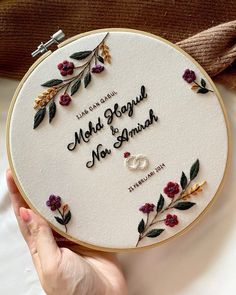 someone is holding up a hand embroidered wedding ring and name on a white hoop with red flowers