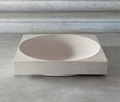 a white bowl sitting on top of a cement slab in front of a wall and window