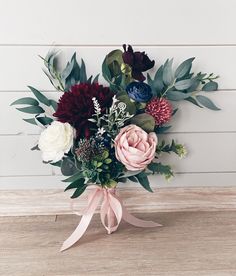 a bouquet of flowers is sitting on a wooden table with a pink ribbon around it