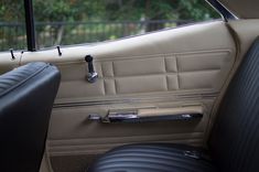 the interior of an old car with black leather seats and chrome door handles, in front of a fenced area