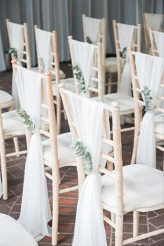 rows of chairs with white sashes and greenery on them