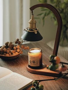 an open book on a table next to a lit candle and bowl of nuts in front of a desk lamp