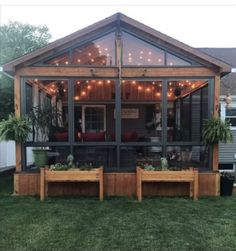 a screened in porch with potted plants and string lights on the roof, surrounded by grass