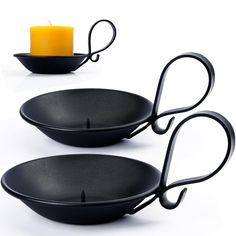 two black bowls with handles are next to a candle holder and a candle on a white background