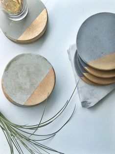 four plates with gold and silver designs on them sitting next to a plant in a glass jar