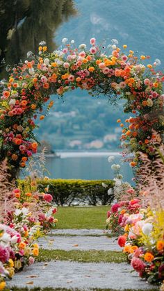 an arch made out of flowers on the side of a road with mountains in the background