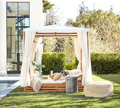 a bed sitting on top of a lush green field next to a swimming pool and covered in white curtains