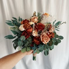 a person holding a bouquet of flowers and greenery in front of a white backdrop